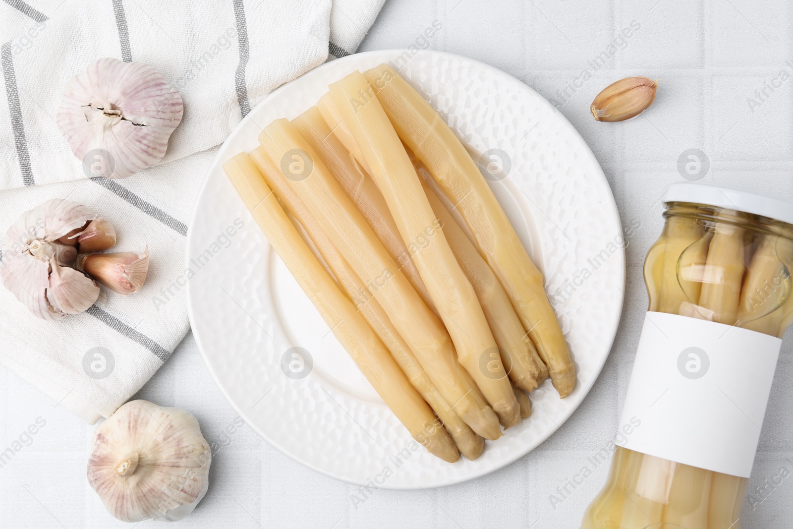 Photo of Pickled asparagus and garlic on white tiled table, flat lay