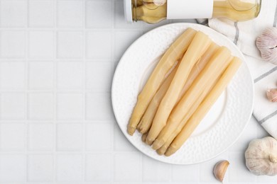 Photo of Pickled asparagus and garlic on white tiled table, flat lay. Space for text