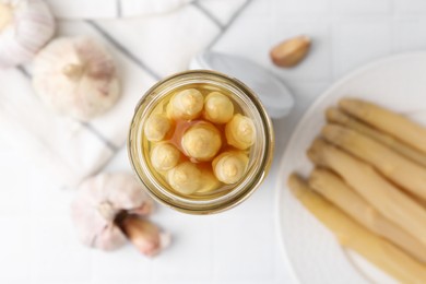Photo of Pickled asparagus and garlic on white tiled table, flat lay