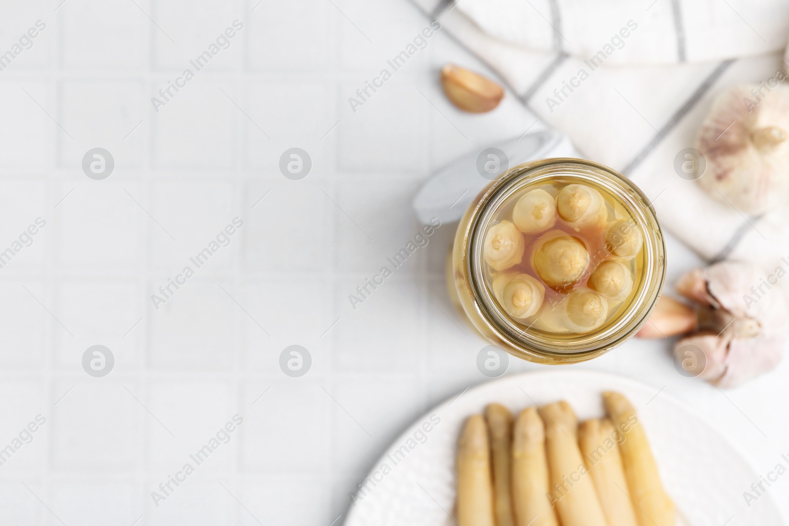 Photo of Pickled asparagus and garlic on white tiled table, flat lay. Space for text