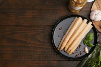 Photo of Pickled asparagus and spices on wooden table, flat lay. Space for text