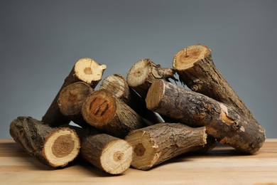 Photo of Pile of cut firewood on wooden table against grey background, closeup