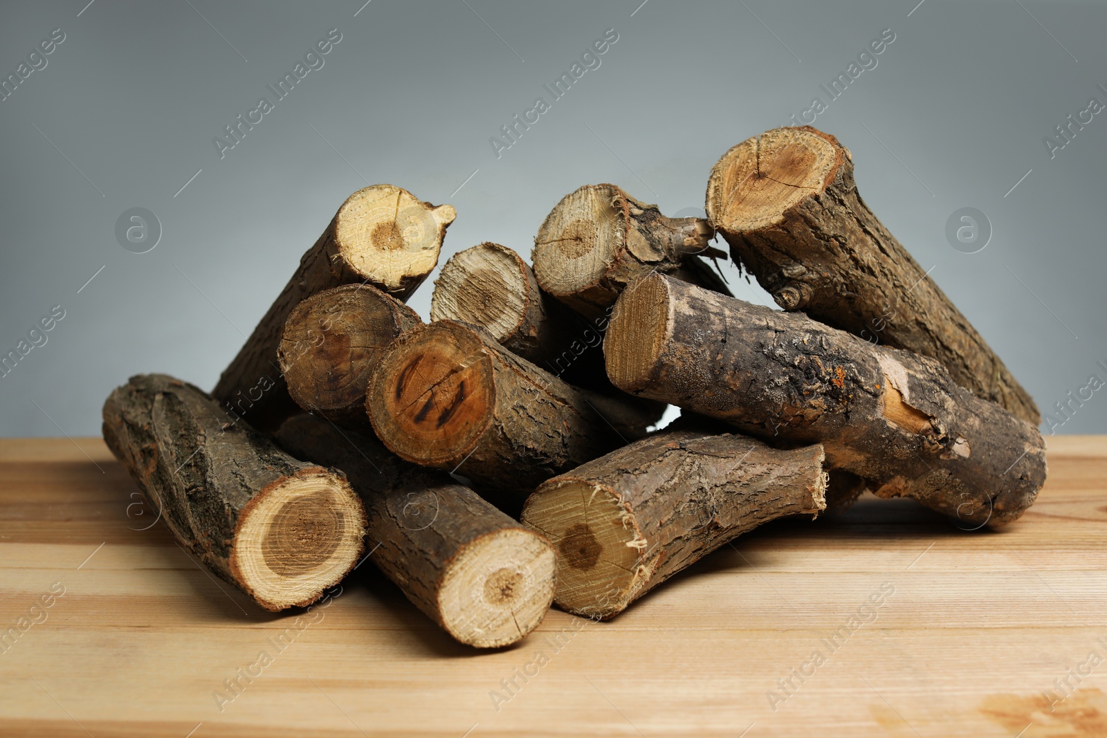 Photo of Pile of cut firewood on wooden table against grey background