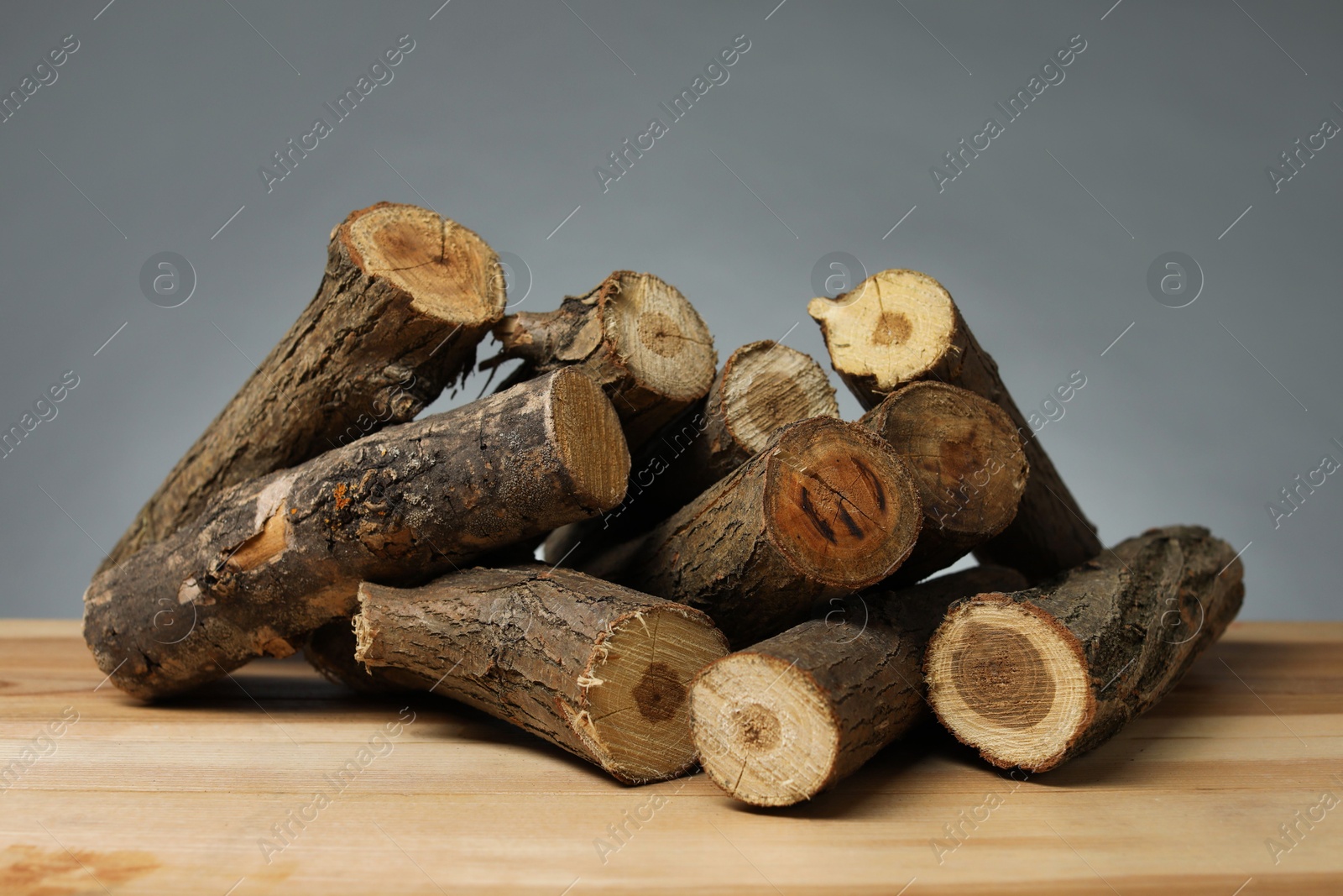 Photo of Pile of cut firewood on wooden table against grey background