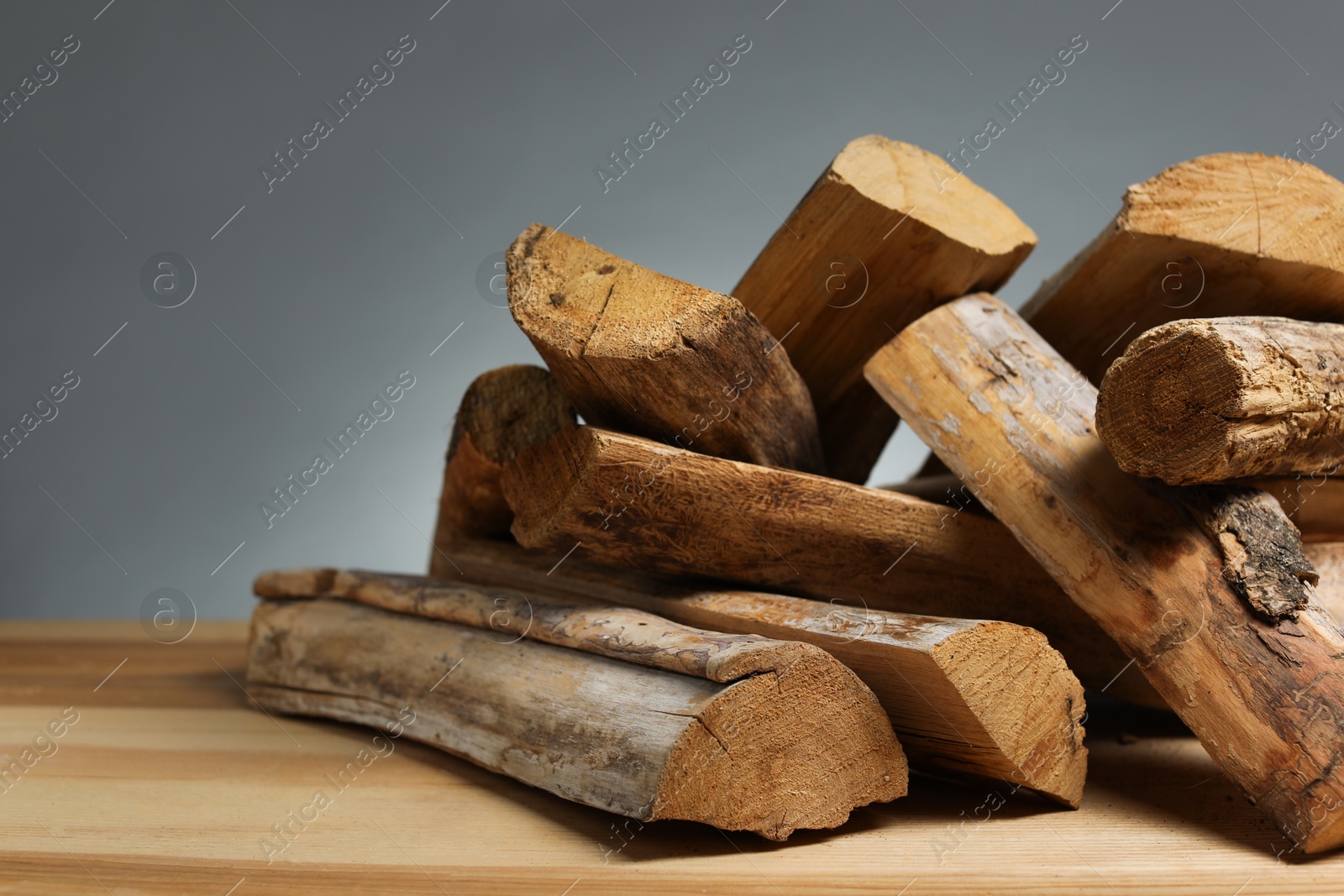 Pile of cut firewood on wooden table against grey background, closeup. Space for text Photo of Pile of cut firewood on wooden table against grey background, closeup. Space for text