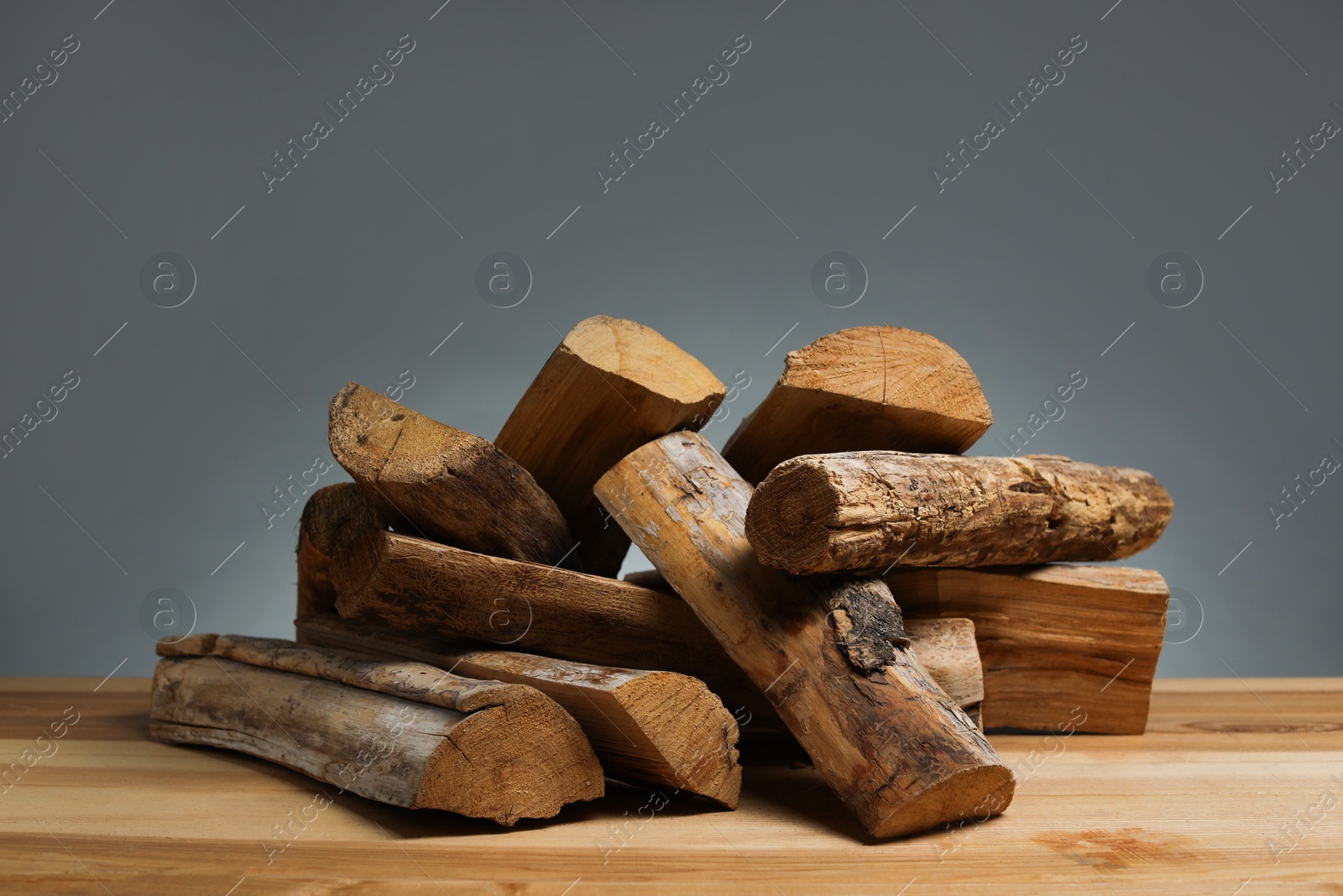 Photo of Pile of cut firewood on wooden table against grey background