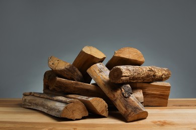 Photo of Pile of cut firewood on wooden table against grey background