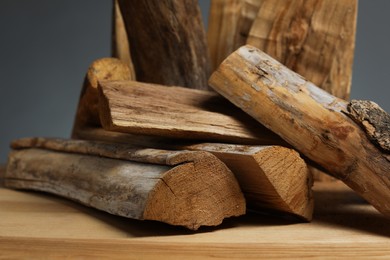 Photo of Pile of cut firewood on wooden table against grey background, closeup