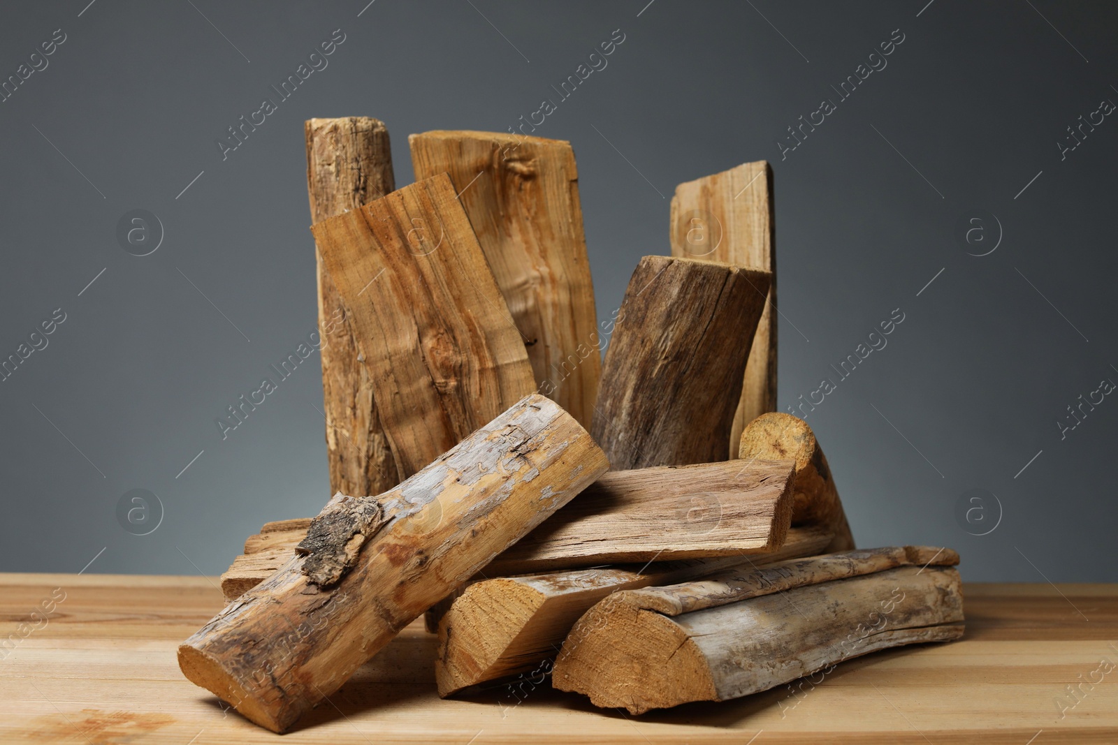 Pile of cut firewood on wooden table against grey background Photo of Pile of cut firewood on wooden table against grey background