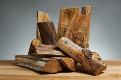 Photo of Pile of cut firewood on wooden table against grey background, closeup