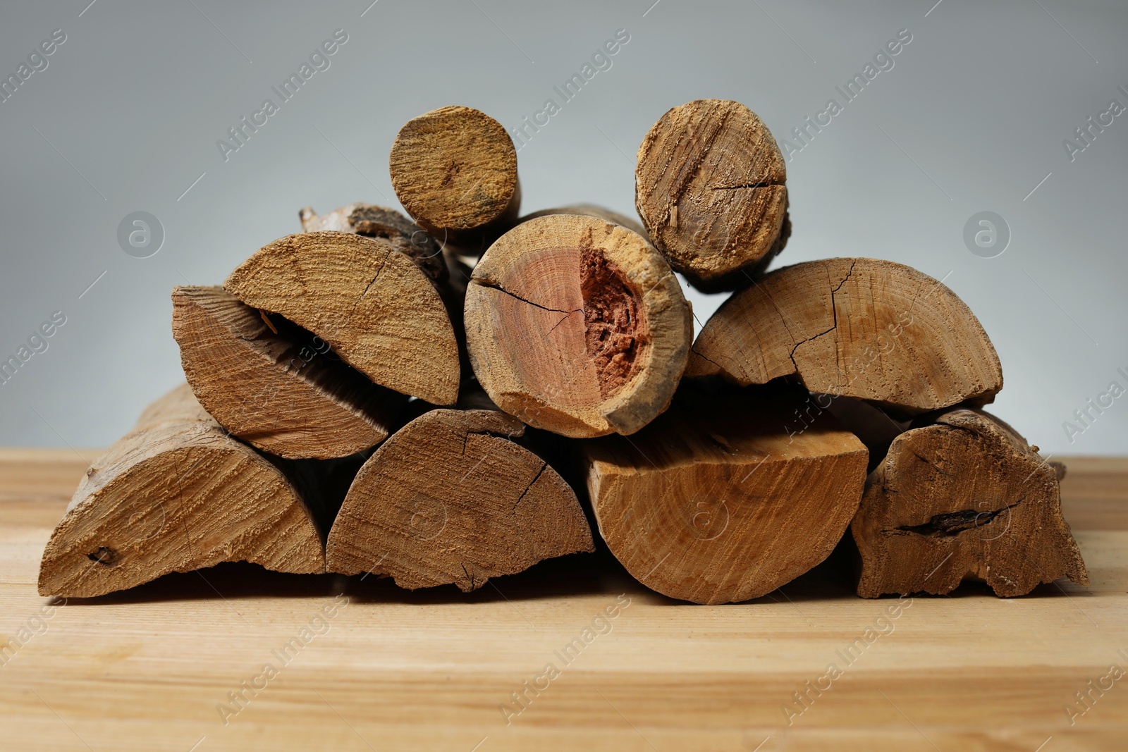 Photo of Pile of cut firewood on wooden table against grey background, closeup