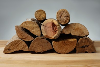 Photo of Pile of cut firewood on wooden table against grey background, closeup