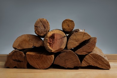Photo of Pile of cut firewood on wooden table against grey background, closeup