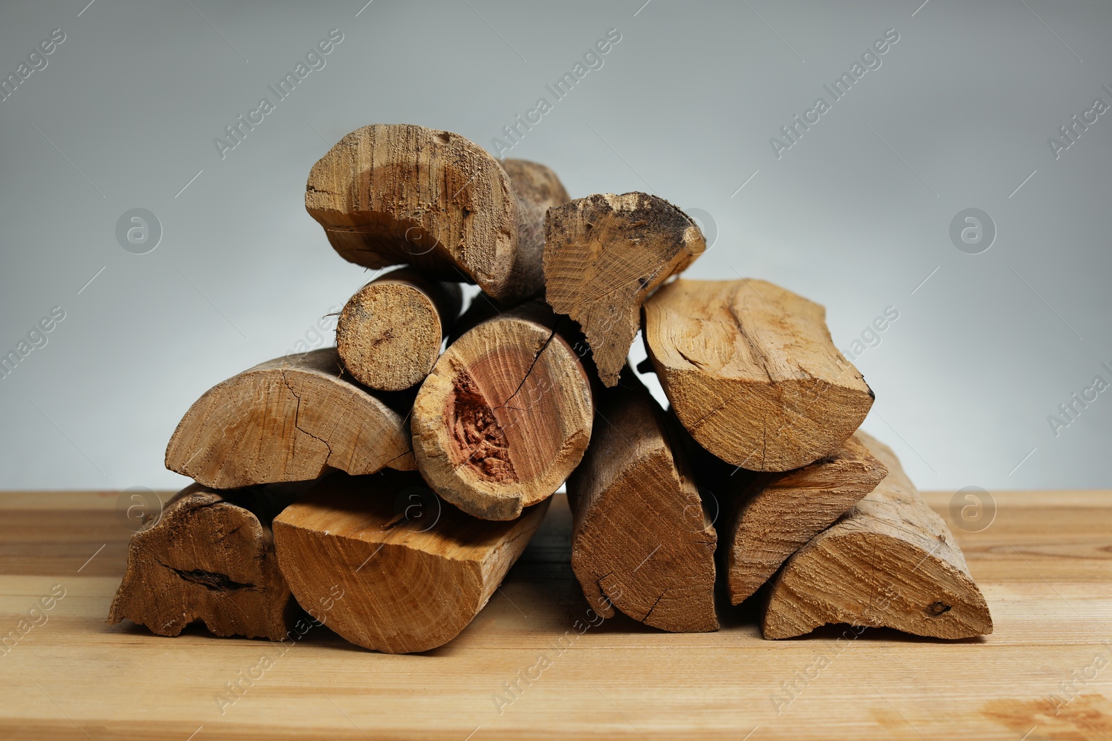 Photo of Pile of cut firewood on wooden table against grey background