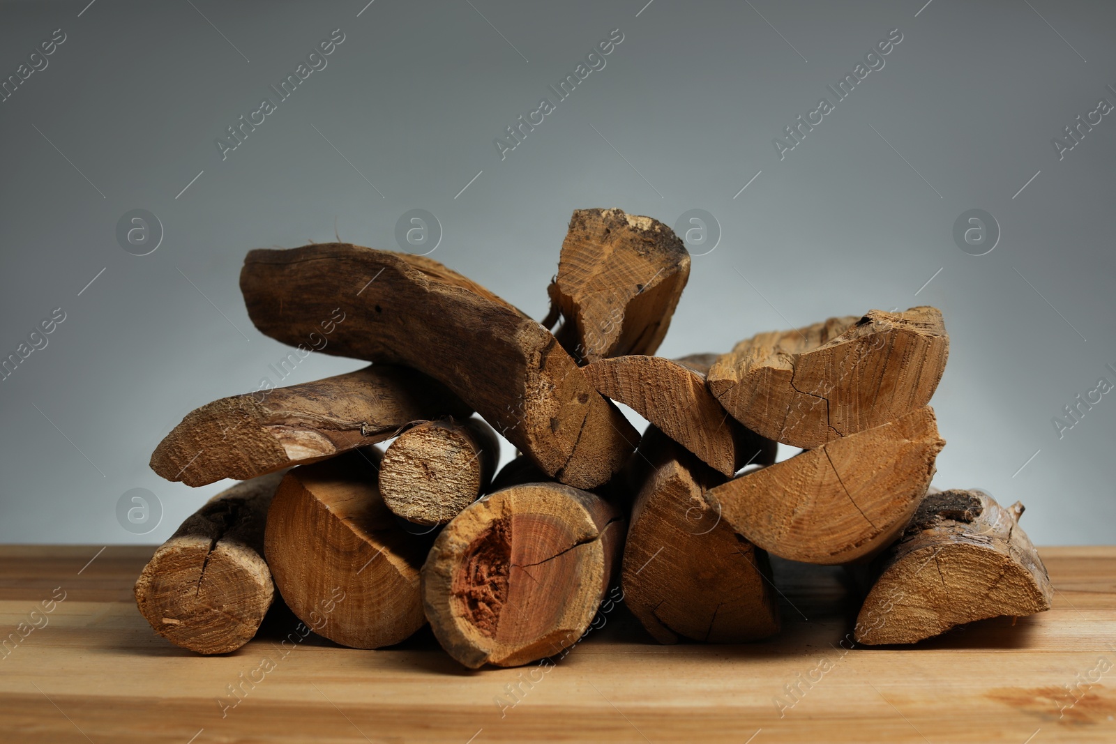 Photo of Pile of cut firewood on wooden table against grey background