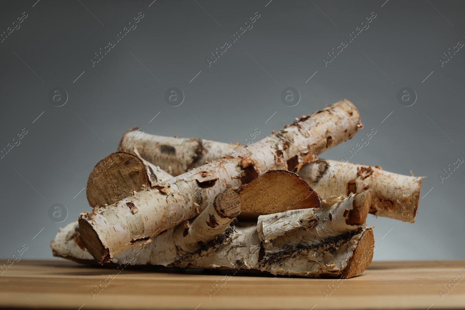 Pile of cut firewood on wooden table against grey background Photo of Pile of cut firewood on wooden table against grey background