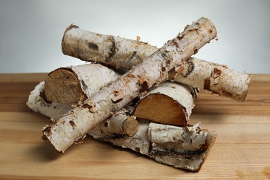 Photo of Pile of cut firewood on wooden table against light grey background, closeup