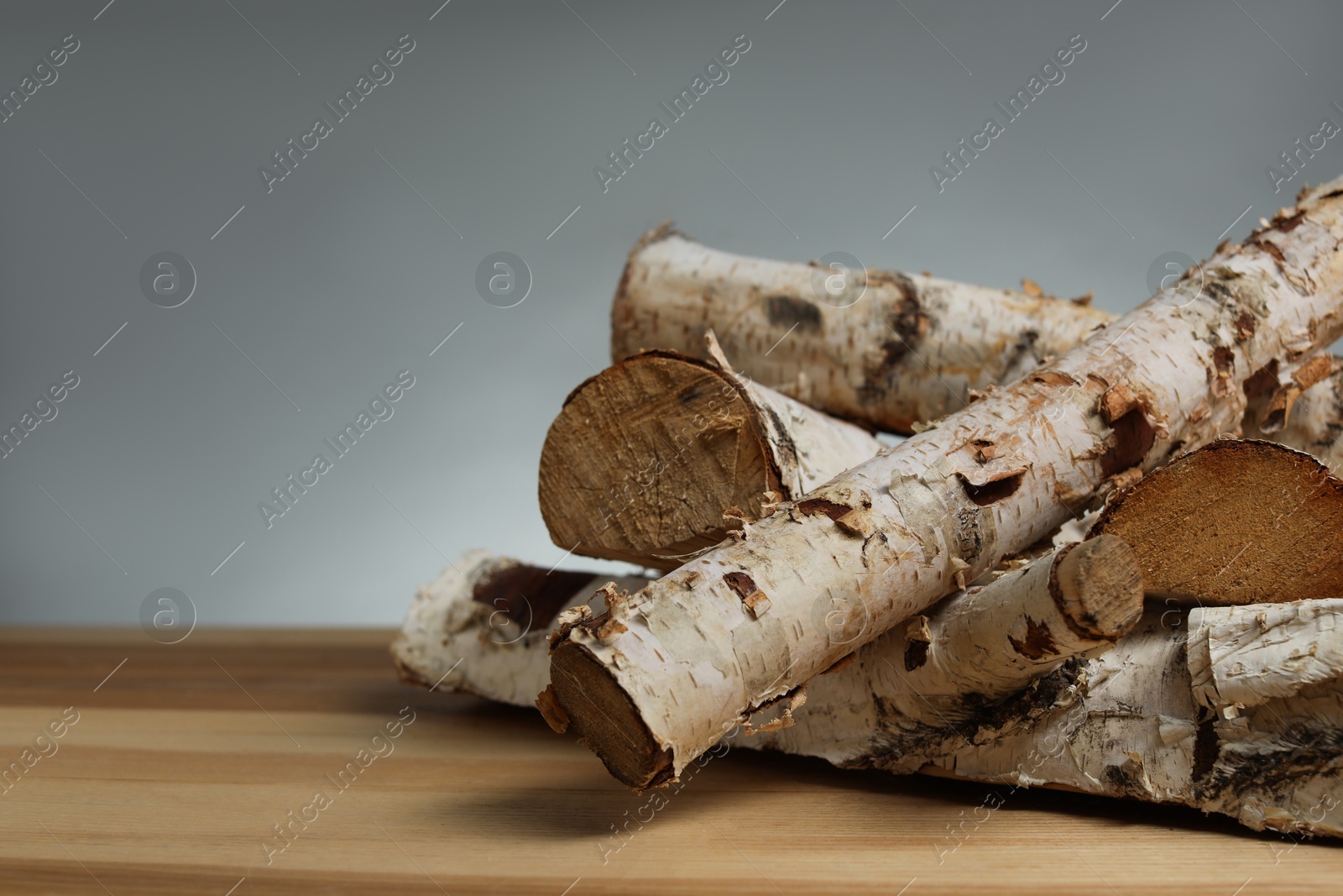Pile of cut firewood on wooden table against grey background, closeup. Space for text Photo of Pile of cut firewood on wooden table against grey background, closeup. Space for text