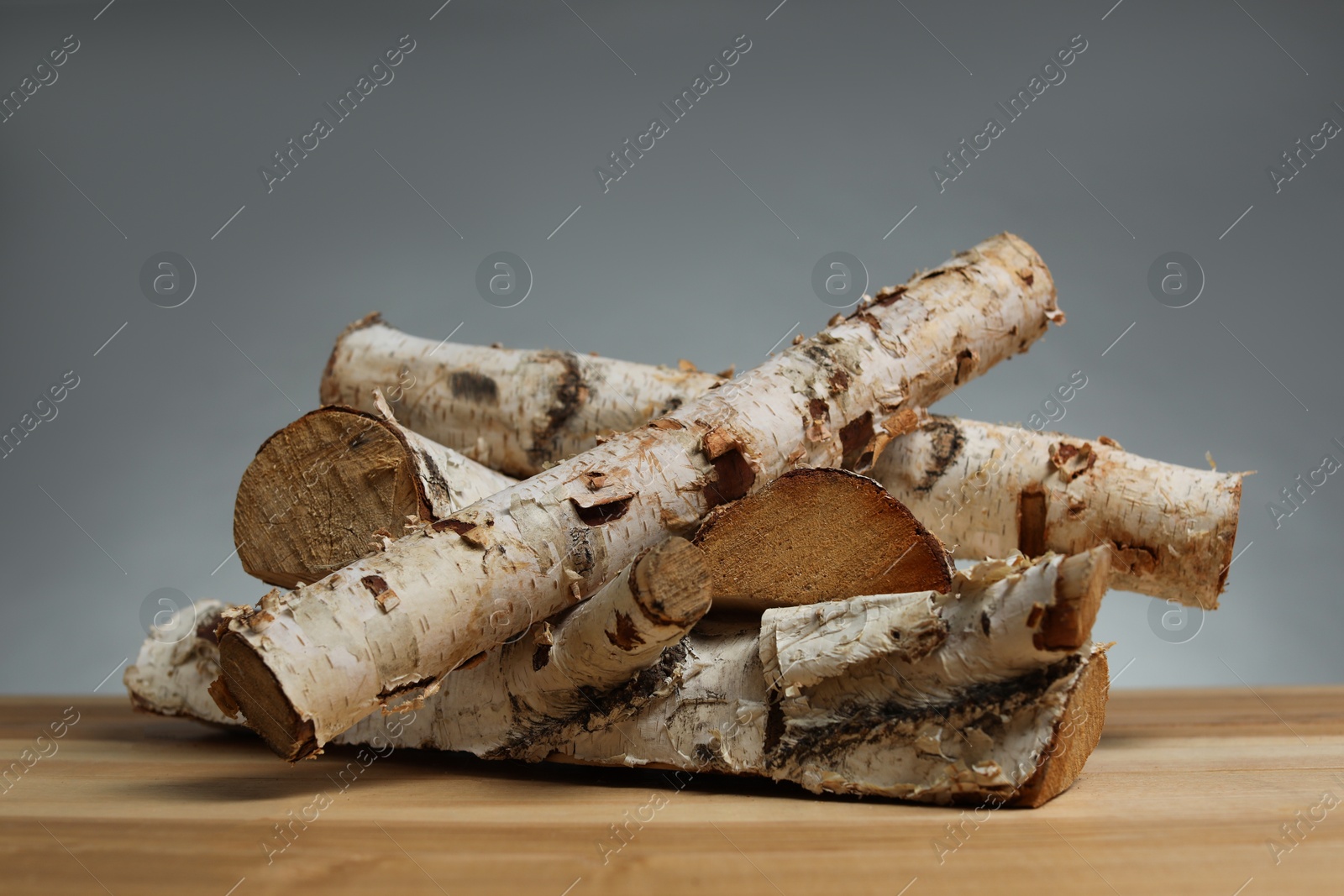 Photo of Pile of cut firewood on wooden table against grey background, closeup