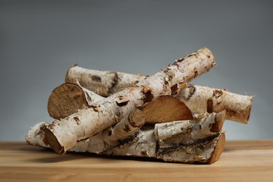 Photo of Pile of cut firewood on wooden table against grey background, closeup
