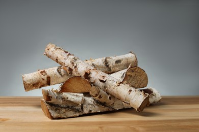 Photo of Pile of cut firewood on wooden table against grey background