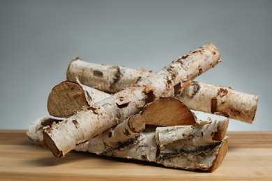 Photo of Pile of cut firewood on wooden table against grey background, closeup