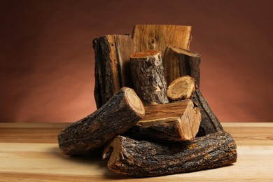Photo of Pile of cut firewood on wooden table against brown background, closeup