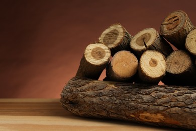 Photo of Pile of cut firewood on wooden table against brown background, closeup. Space for text