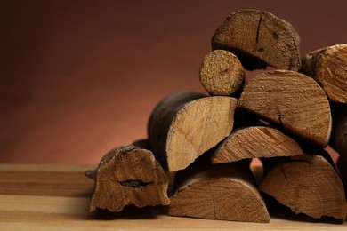 Photo of Pile of cut firewood on wooden table against brown background, closeup. Space for text
