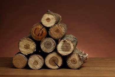 Photo of Pile of cut firewood on wooden table against brown background