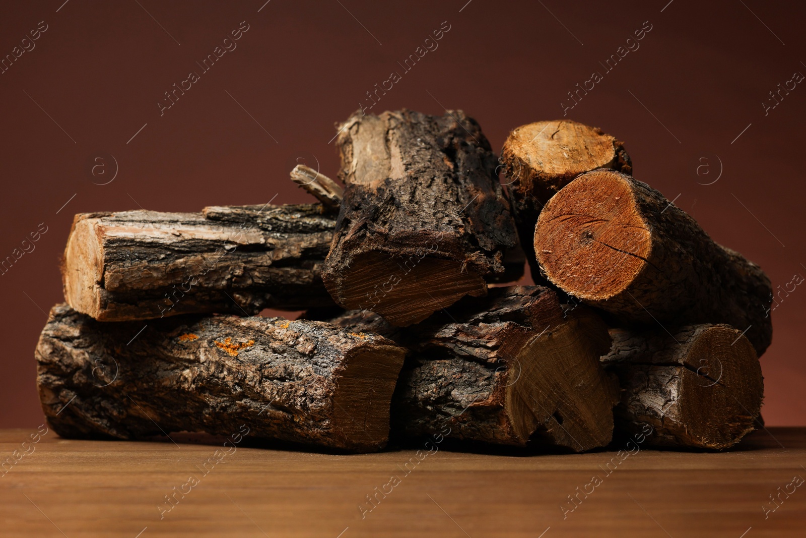 Photo of Pile of cut firewood on wooden table against brown background