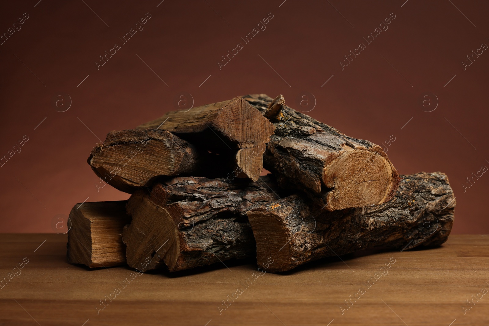 Photo of Pile of cut firewood on wooden table against brown background
