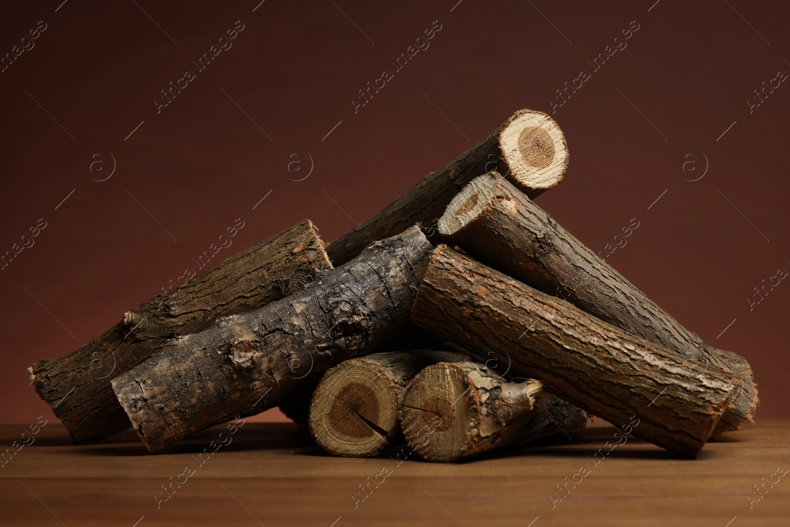 Photo of Pile of cut firewood on wooden table against brown background