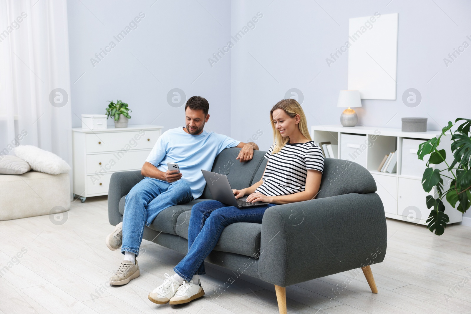 Photo of Happy couple with devices spending time together on sofa at home