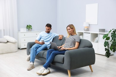 Photo of Happy couple with devices spending time together on sofa at home