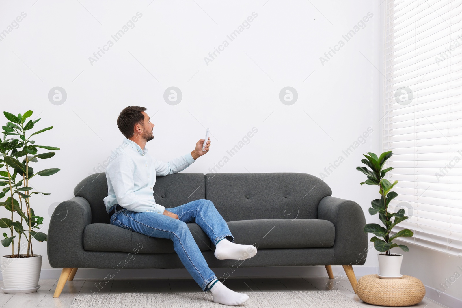 Man using remote to control air conditioner on sofa at home. Space for text Photo of Man using remote to control air conditioner on sofa at home. Space for text