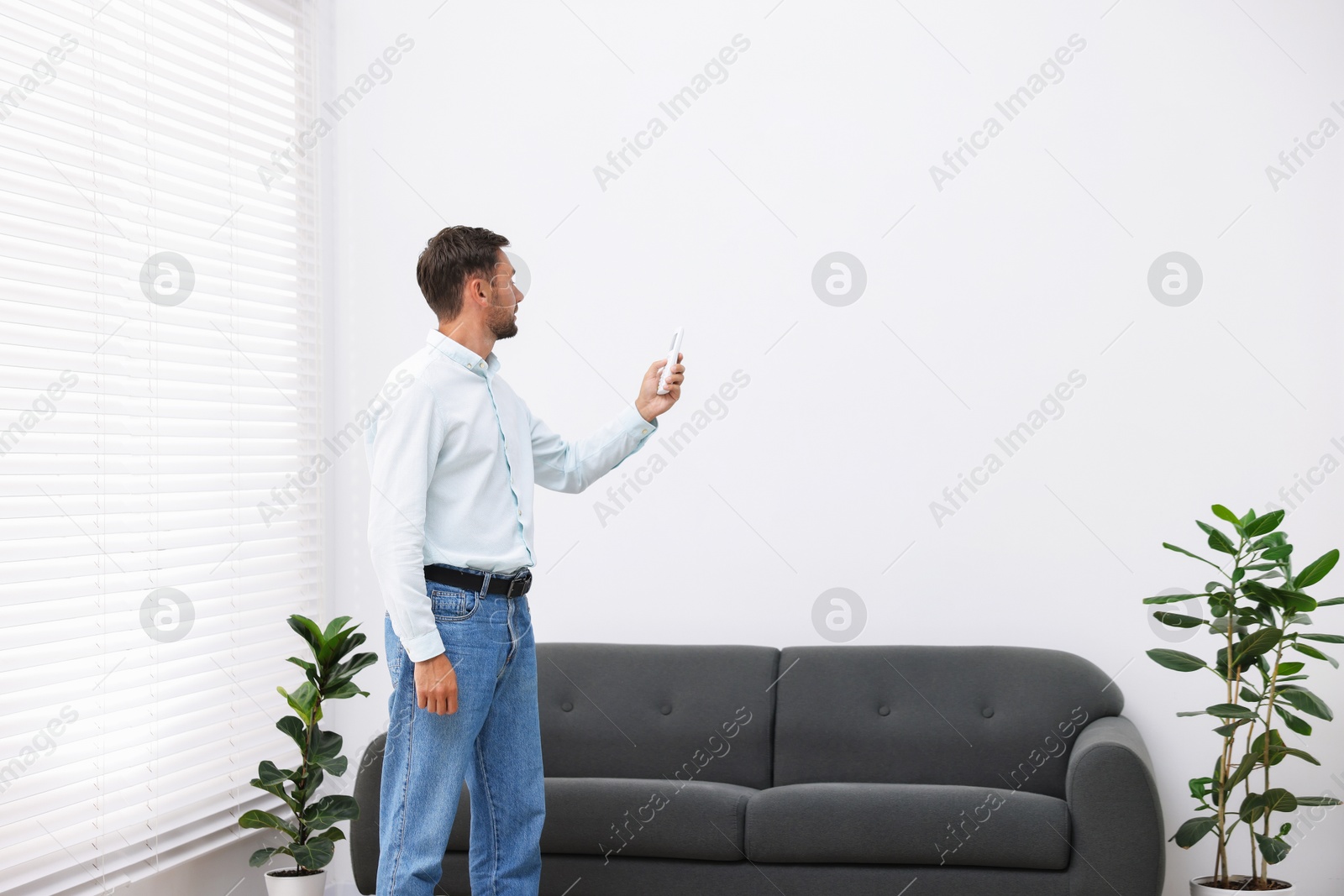 Man using remote to control air conditioner at home. Space for text Photo of Man using remote to control air conditioner at home. Space for text