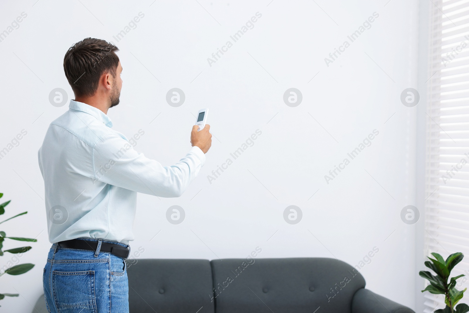 Man using remote to control air conditioner at home. Space for text Photo of Man using remote to control air conditioner at home. Space for text