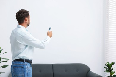 Photo of Man using remote to control air conditioner at home. Space for text