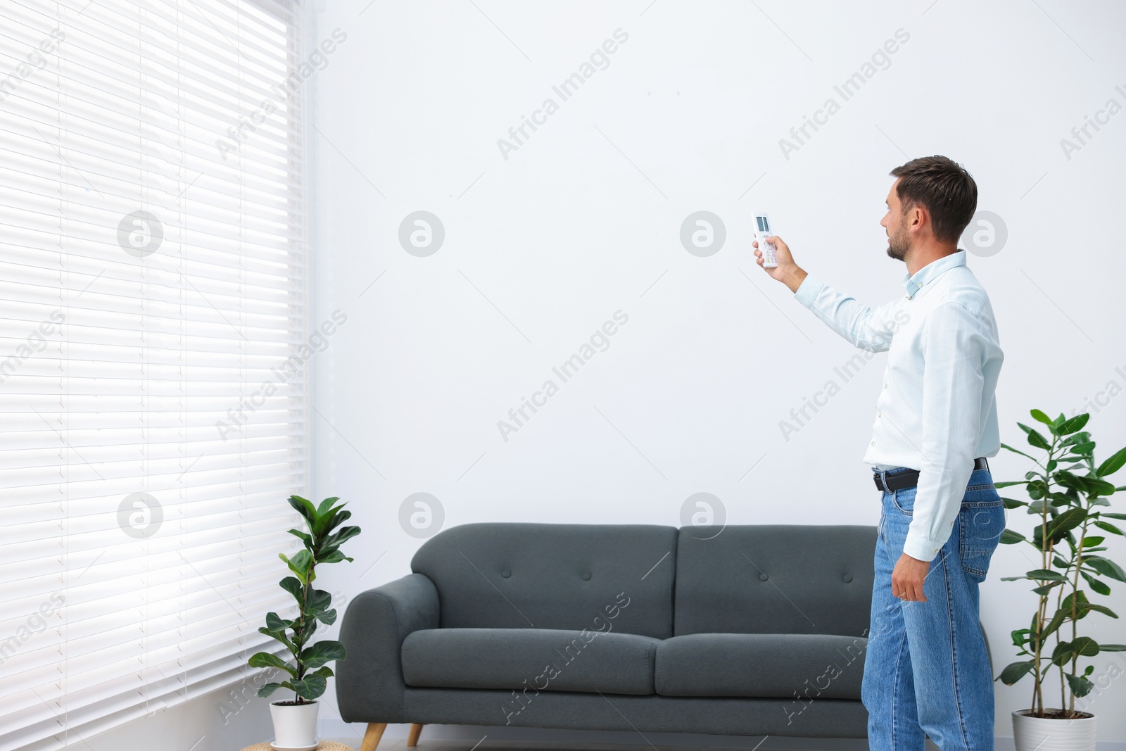 Man using remote to control air conditioner at home. Space for text Photo of Man using remote to control air conditioner at home. Space for text