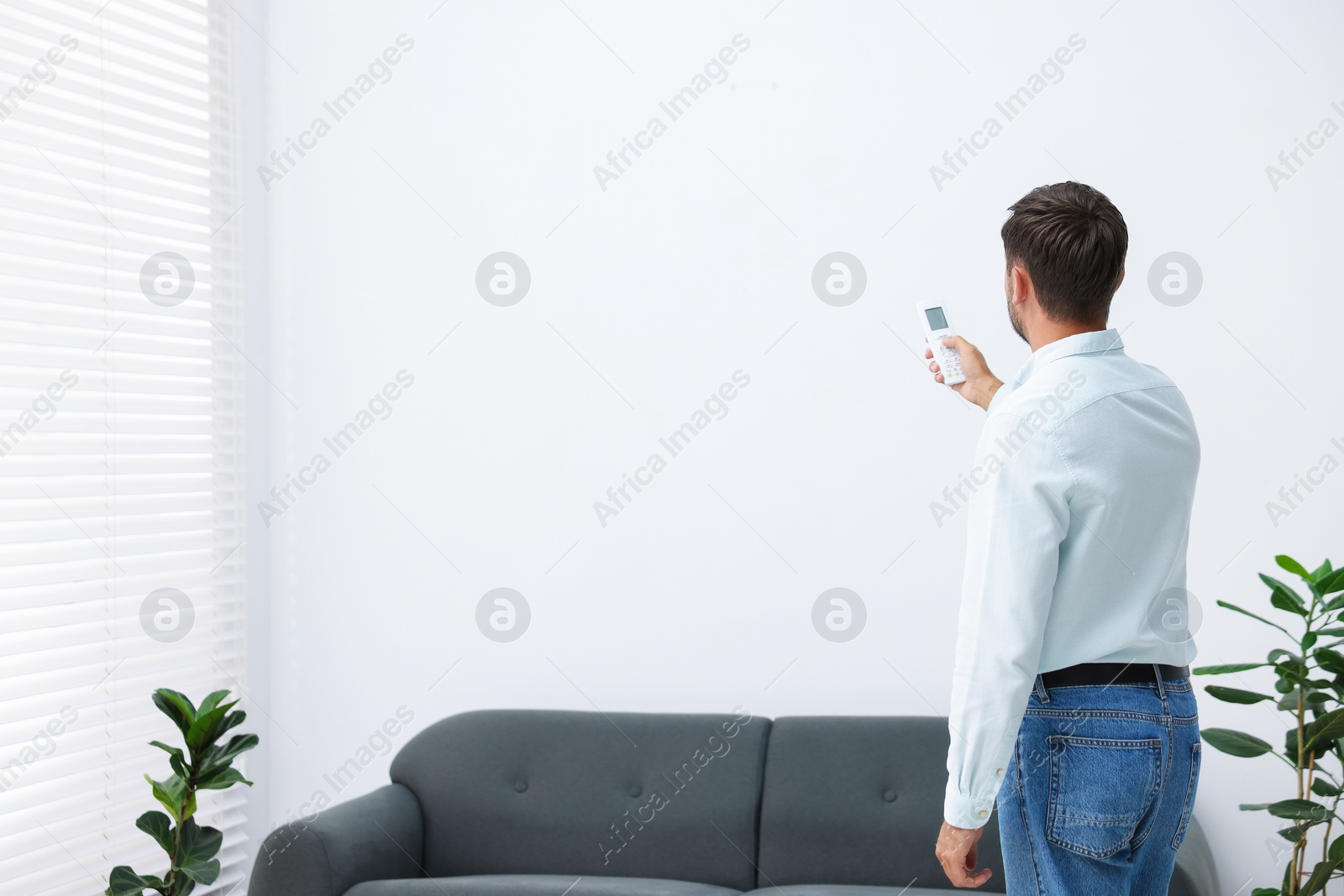 Man using remote to control air conditioner at home, back view. Space for text Photo of Man using remote to control air conditioner at home, back view. Space for text