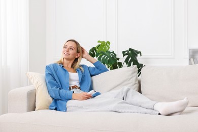 Photo of Woman with air conditioner remote control on sofa at home