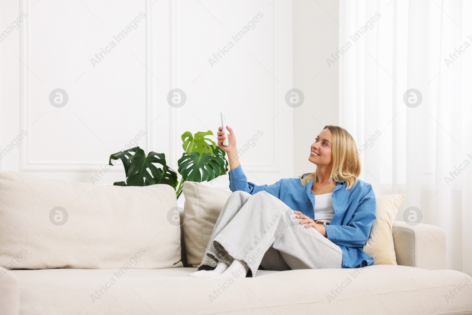 Woman using remote to control air conditioner on sofa at home Photo of Woman using remote to control air conditioner on sofa at home