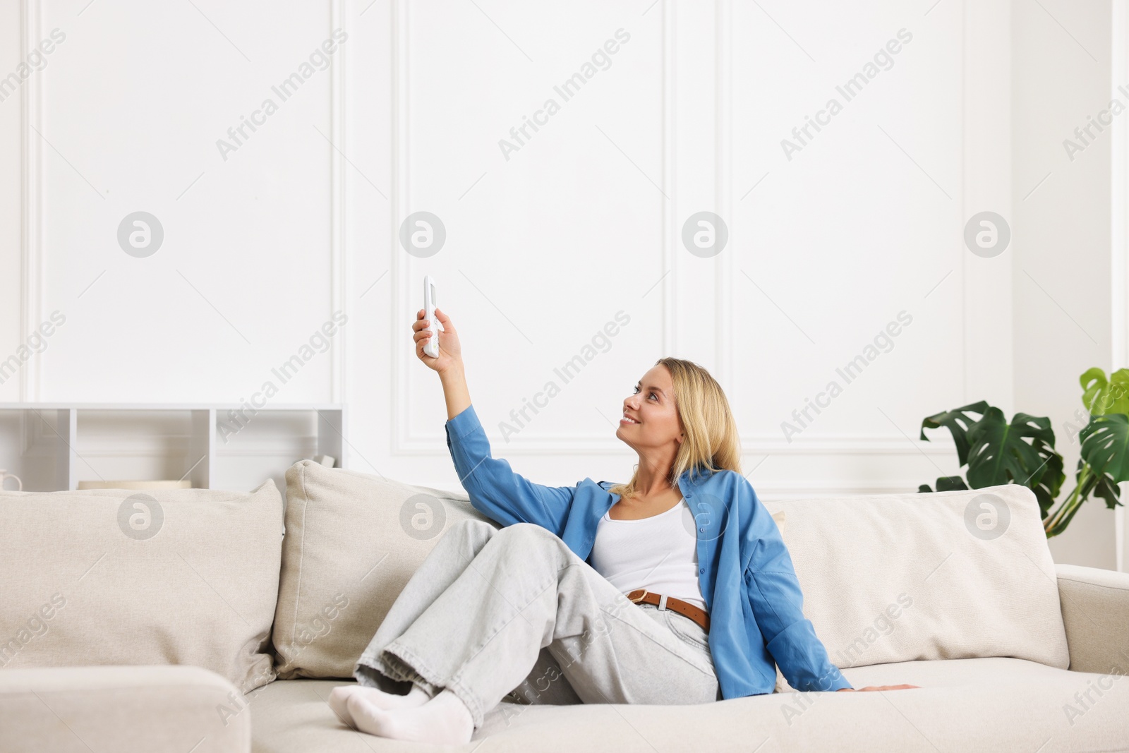 Woman using remote to control air conditioner on sofa at home Photo of Woman using remote to control air conditioner on sofa at home