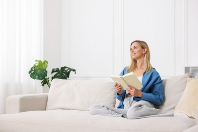 Photo of Woman reading book on sofa at home. Space for text