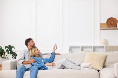 Photo of Couple using remote to control air conditioner on sofa at home. Space for text