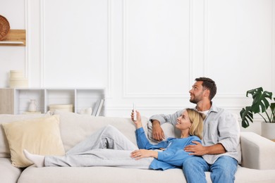 Photo of Couple using remote to control air conditioner on sofa at home. Space for text