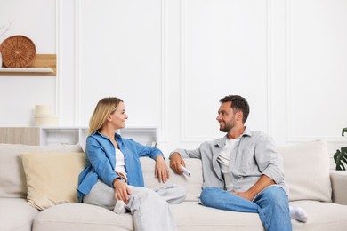 Photo of Couple with air conditioner remote control on sofa at home