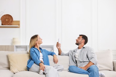 Photo of Couple using remote to control air conditioner on sofa at home