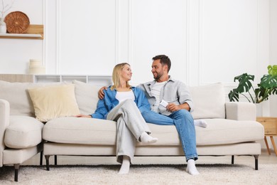 Photo of Couple with air conditioner remote control on sofa at home